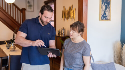 Salesman in navy polo using ipad to show room layout to female homeowner.